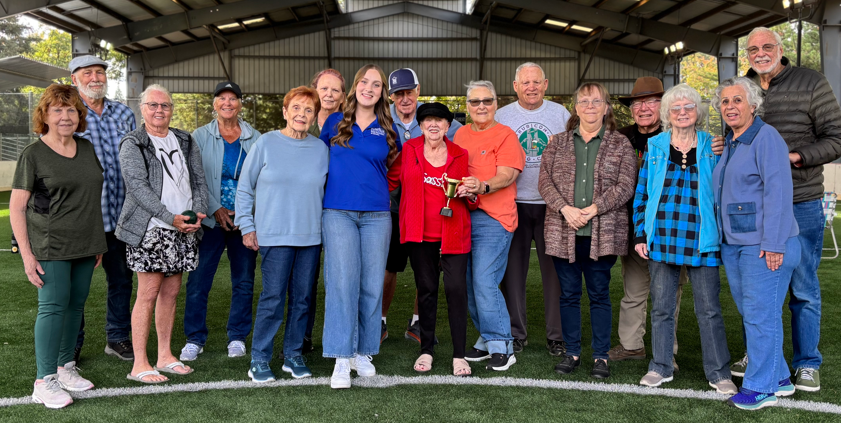 Group of older adults standing on turf field holding a trophy