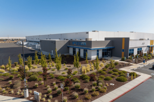 A modern industrial building with a landscaped area in front and a clear blue sky above.