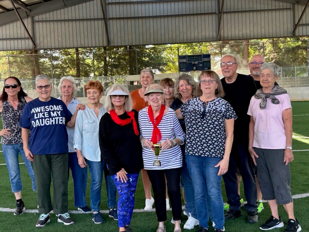 A group of older adults on a turf field holding a trophy