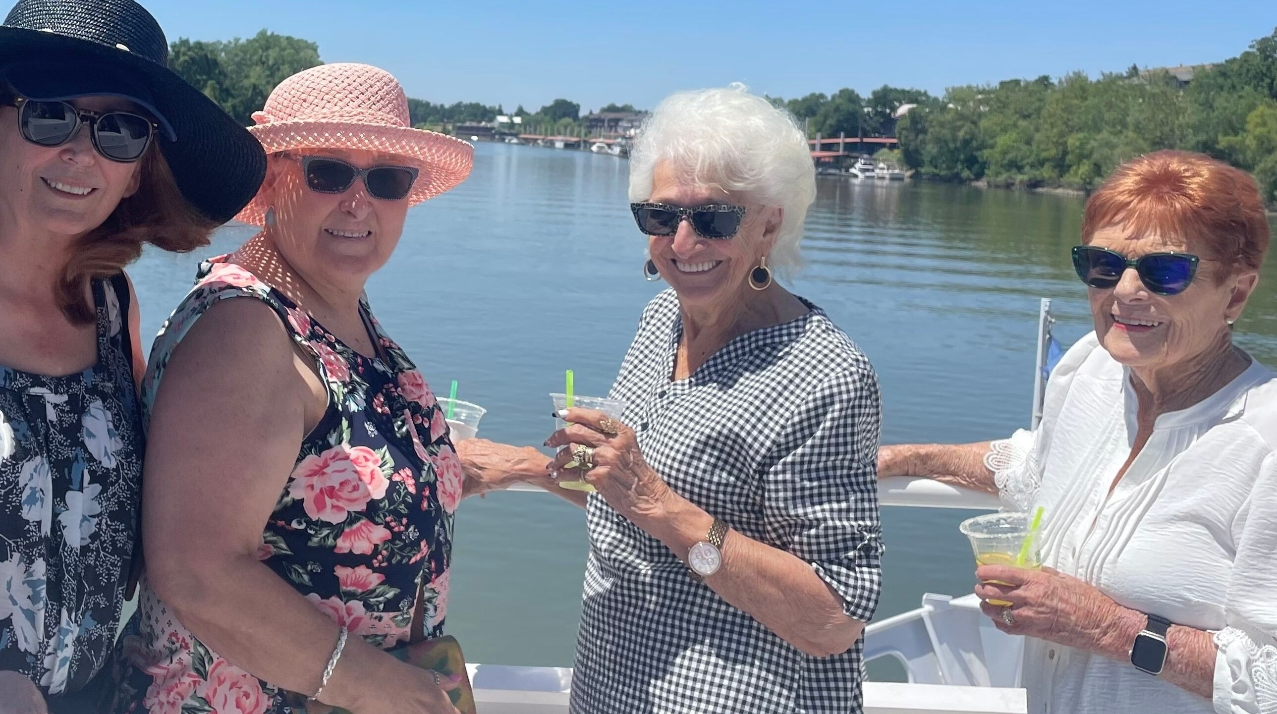 4 women on a boat on a lake holding drinks and smiling