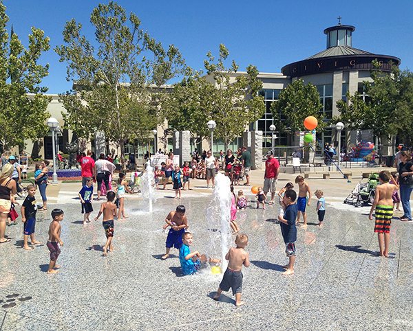 Kids playing in the Vernon Street Town Square splash pad in downtown Roseville, with the Civic Center behind