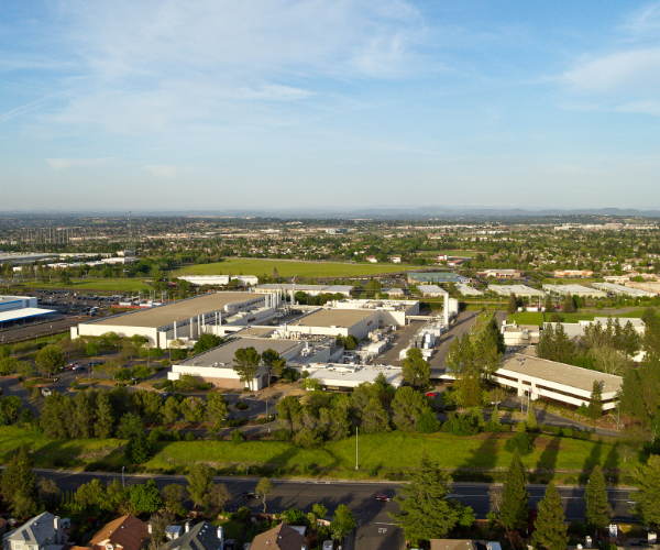 Aerial view of a large campus for Bosch  with modern buildings, parking areas, landscaped green trees, and surrounding neighborhoods under a partly cloudy blue sky.