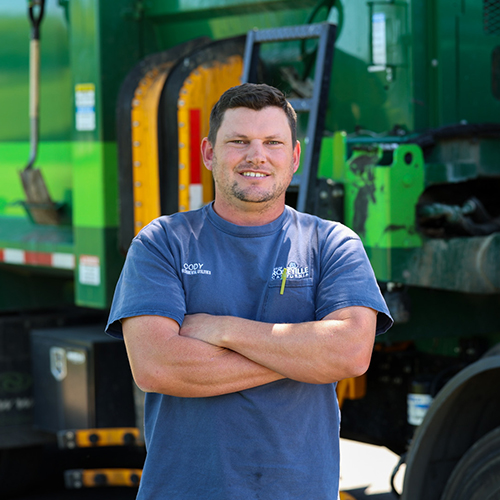 A truck driver stands outside in front of his garbage truck