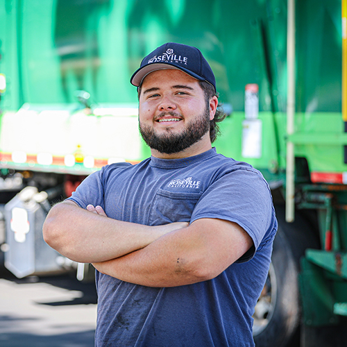 A truck driver stands outside in front of his garbage truck