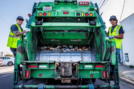 Garbage truck collecting waste with two workers standing on the back during pickup