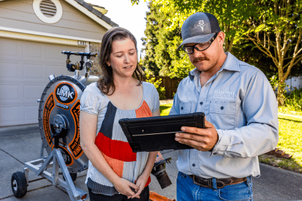 Utility worker reviewing information on a tablet with a resident in a driveway near maintenance equipment