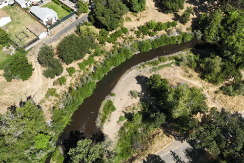 Aerial view of a winding creek flowing through a landscape with trees and houses on the left bank. (1)
