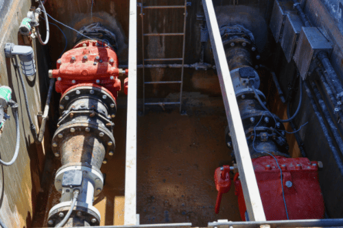 Two large water pipes with red casings and metal pipes in a concrete enclosure.