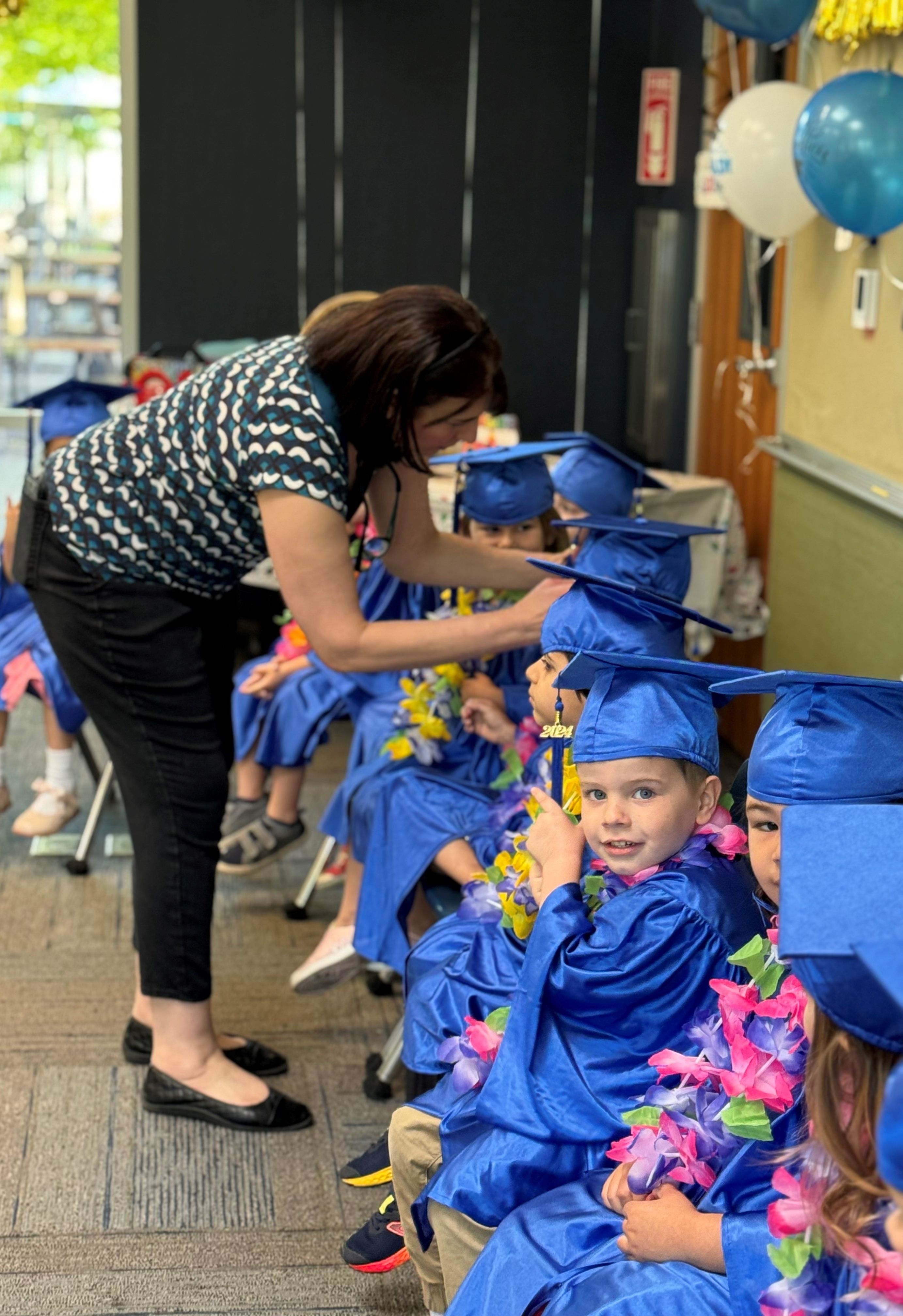 preschool aged children seated in a row with graduation caps and gowns
