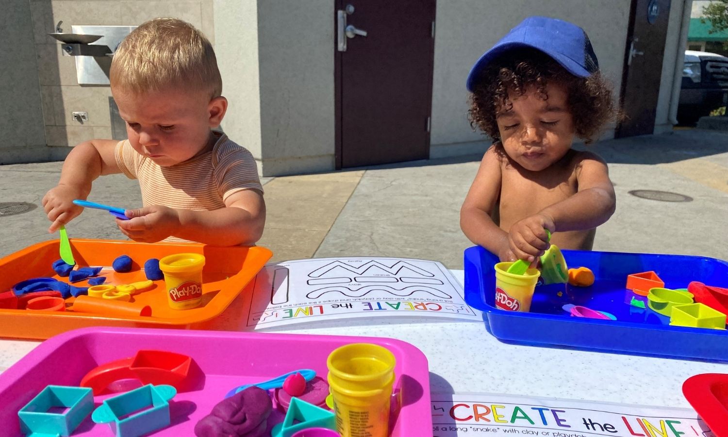 Tot Tuesday. Image of 2 tots playing with Play Doh, outside