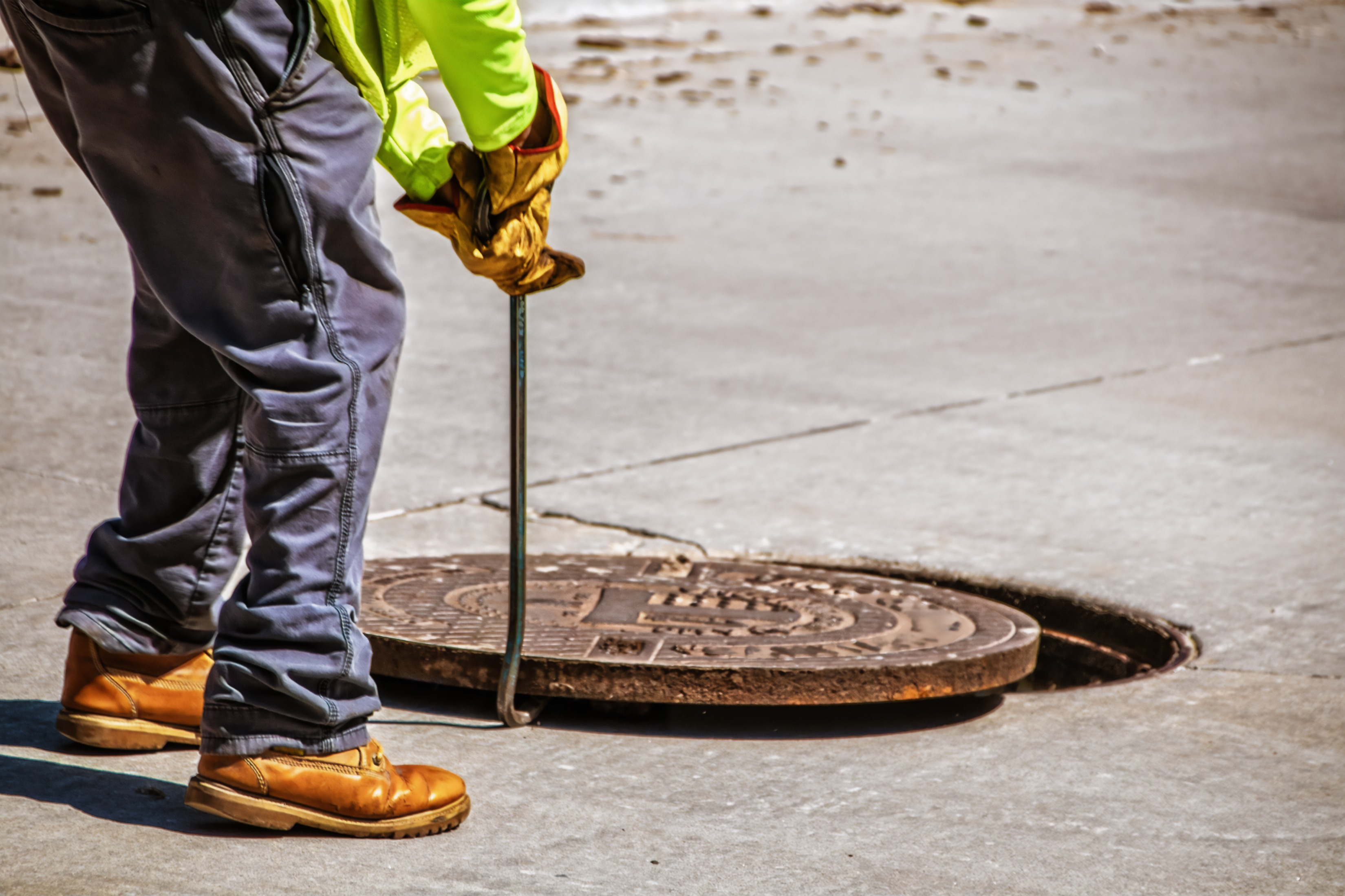 Construction worker lifts a manhole cover