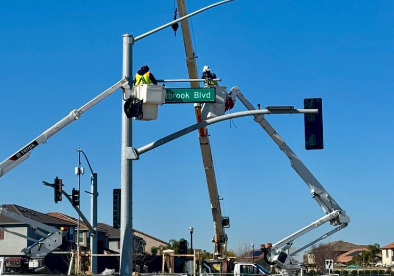 Two construction workers in raised buckets install a traffic signal.