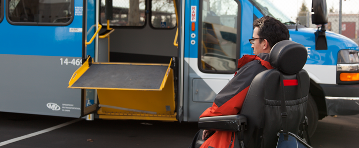 A ramp unfolds from a bus for a waiting passenger in a wheelchair.