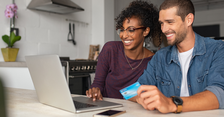 Smiling couple looking at laptop with credit card in hand