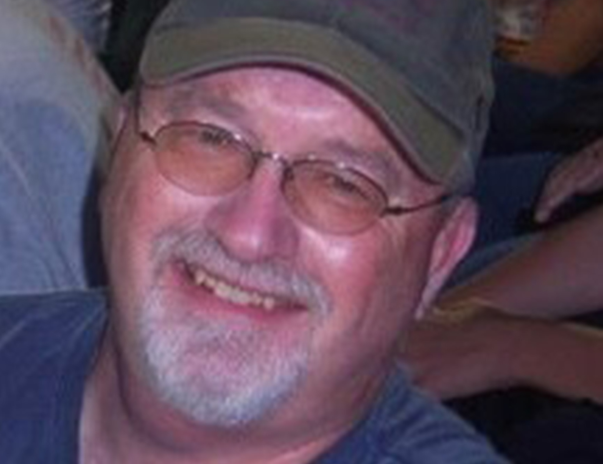 Man with a goatee smiling while wearing glasses and a green ballcap