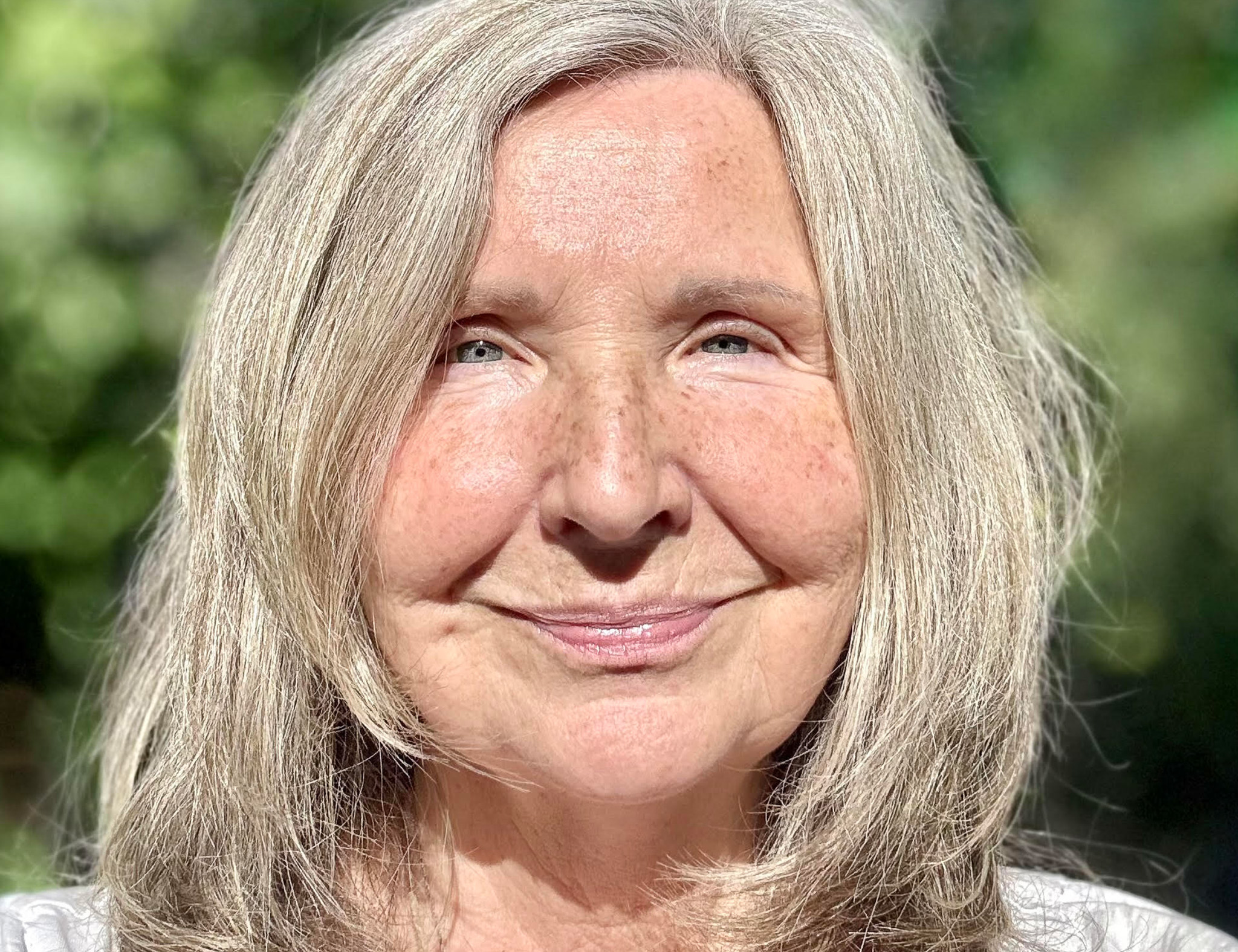 Close up of older woman softly smiling outside in the sun