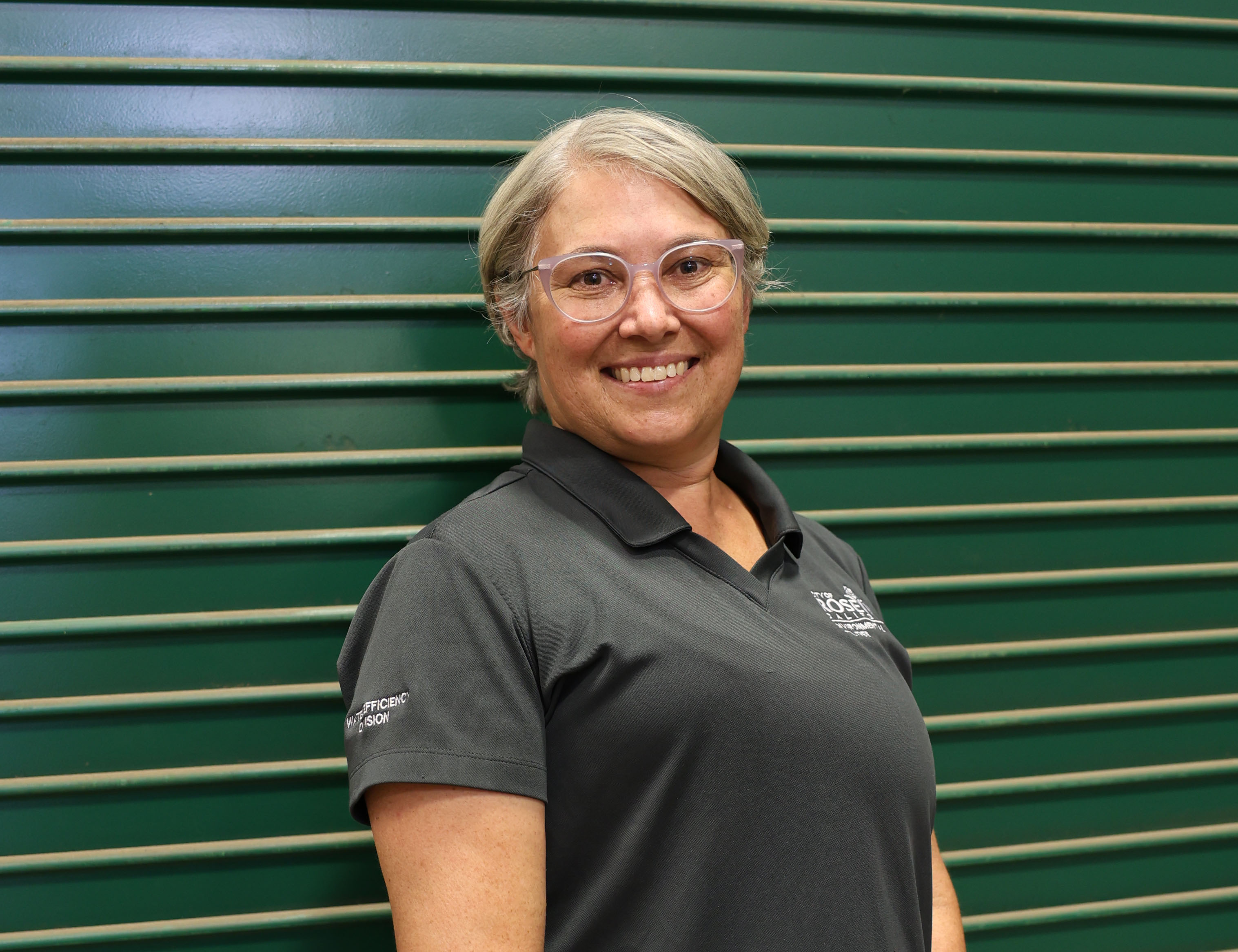 Posed photo of female utility worker standing indoors next to a green garage door