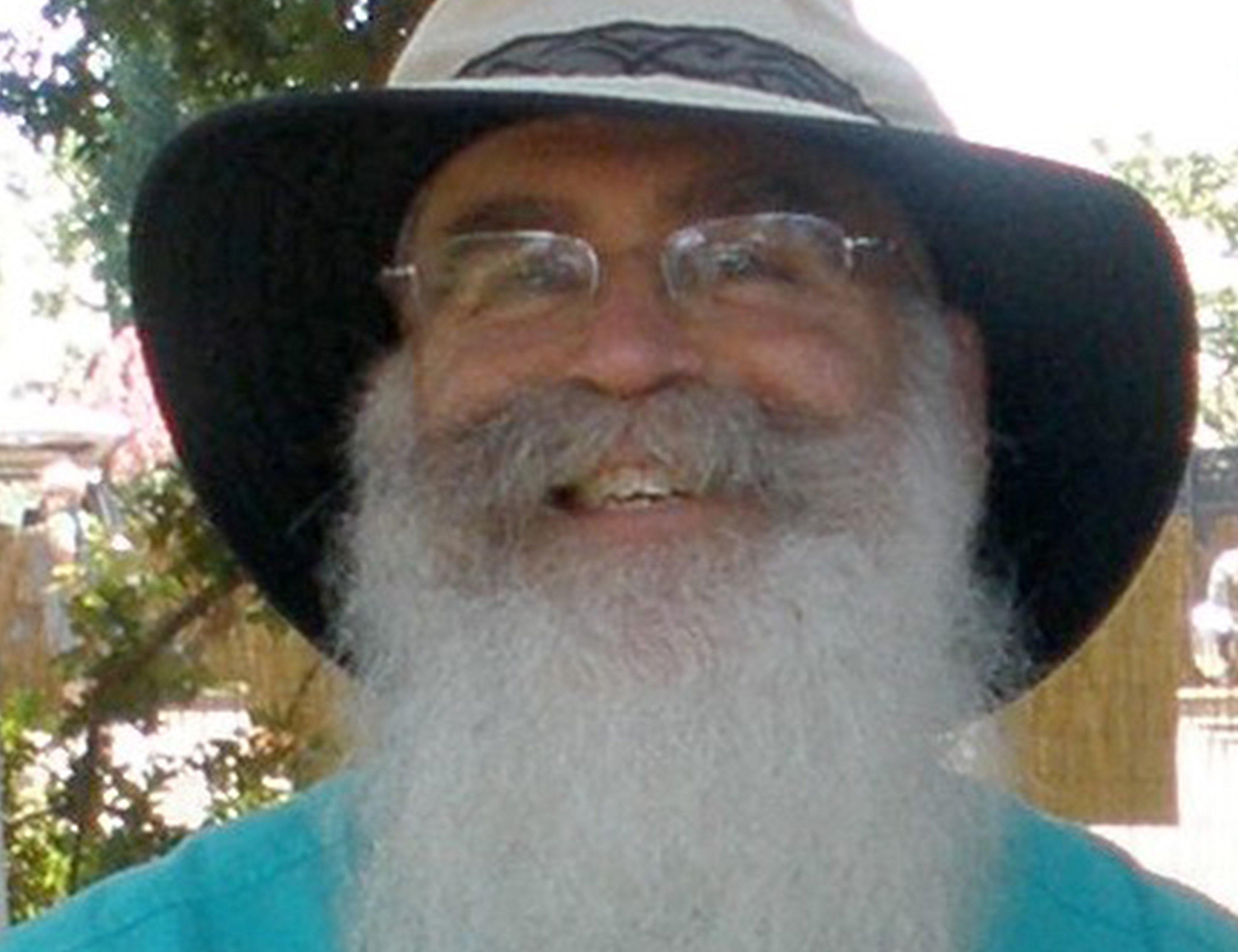 Bearded man smiling while wearing glasses and a bucket hat.