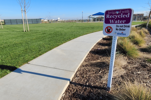 Recycled water sign in a park with grass and a sidewalk and landscaping
